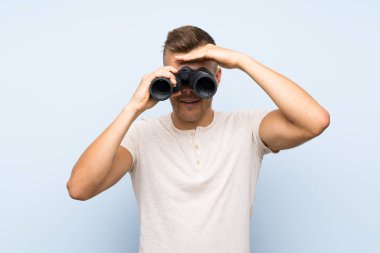 Siyah dürbün ile izole mavi arka plan üzerinde Genç yakışıklı sarışın adam