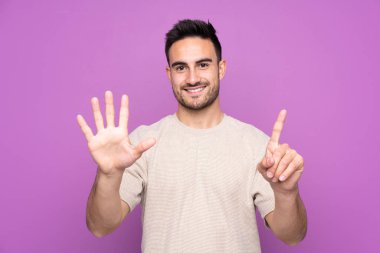 İzole edilmiş mor arka planı olan genç yakışıklı adam parmakları olan altı kişi sayıyor.