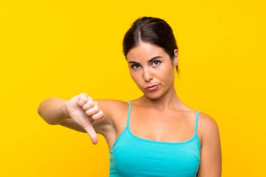 Izole sarı arka plan üzerinde genç kadın başparmak aşağı işareti gösteren