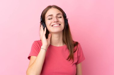 Soyutlanmış pembe arka planda müzik dinleyen genç bir kadın.