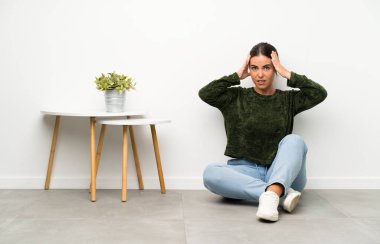 Genç bir kadın yerde oturuyor ve yüzünde sürpriz bir ifade var.