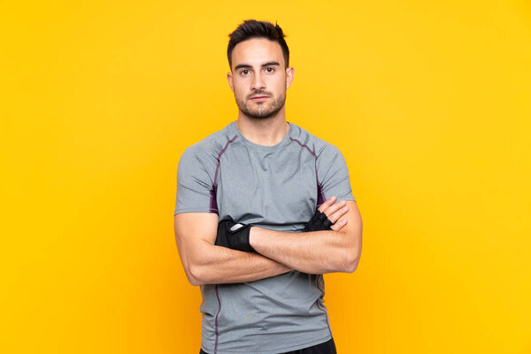 Sport man over isolated yellow wall with arms crossed