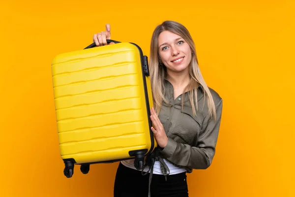 年轻的金发女子带着旅行箱在孤立的黄色背景下度假 — 图库照片