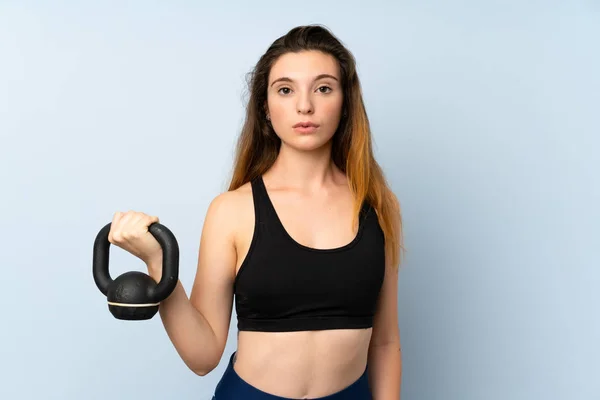 Chica morena joven haciendo levantamiento de pesas con kettlebell sobre fondo aislado —  Fotos de Stock