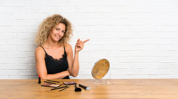 Young Woman Lots Makeup Brush Table Pointing Finger Side — 스톡 사진