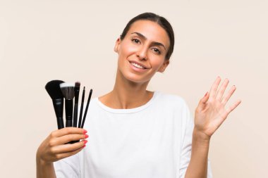 Bir sürü makyaj fırçası tutan genç bir kadın. Mutlu bir ifadeyle selamlıyor.