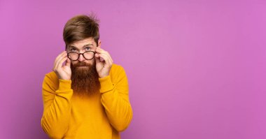 Kızıl saçlı, uzun sakallı, gözlüklü ve şaşırmış bir adam.