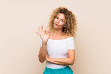 Kıvırcık saçlı, izole edilmiş arka planı olan genç sarışın kadın parmaklarıyla işaret veriyor.