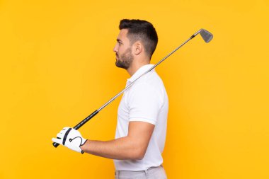 İzole edilmiş sarı arka planda golf oynayan bir adam.