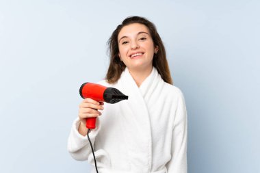 Saç kurutma makineli bornozlu genç bir kadın çok gülümsüyor.