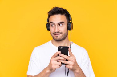 Sarı arka planda genç bir adam cep telefonuyla müzik dinliyor ve düşünüyor.