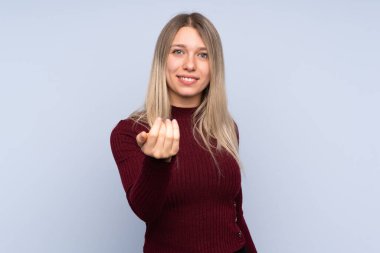 Izole mavi arka plan üzerinde genç sarışın kadın el ile gelmeye davet ediyor. Geldiğin için mutluyum.