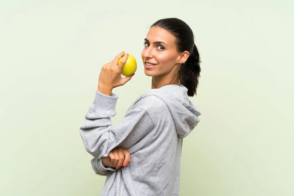 Молодая спортсменка с яблоком на изолированном зеленом фоне — стоковое фото
