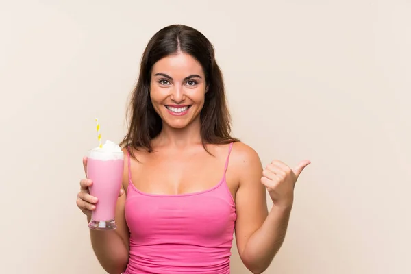 イチゴミルクセーキを持つ若い女性が製品を提示する側を指している — ストック写真