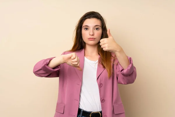 Young brunette girl with blazer over isolated background making good-bad sign. Undecided between yes or not