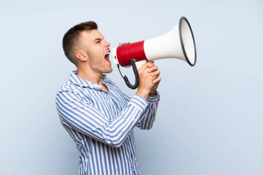Bir megafon ile bağırarak izole mavi arka plan üzerinde Genç yakışıklı sarışın adam