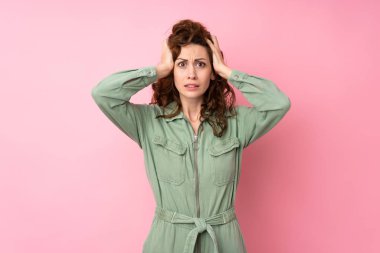 Soyutlanmış pembe arka planda genç ve güzel bir kadın hayal kırıklığına uğradı ve ellerini başının üstüne koydu.