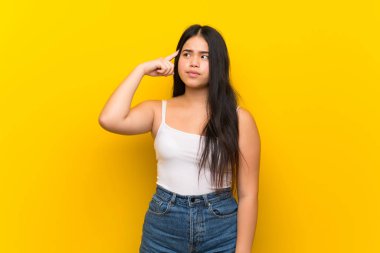 Genç Asyalı kız izole edilmiş sarı arka planda deliliğin hareketini yapıyor. Parmağını kafaya koyuyor.