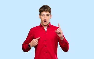 İzole edilmiş mavi arka planda, şaşırmış yüz ifadesi olan yakışıklı bir genç.