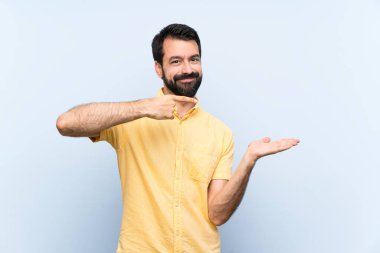 Mavi arka planda sakallı genç bir adam, bir ilan vermek için avucunda hayali bir şey tutuyor.