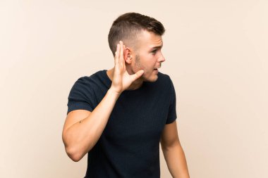 Genç yakışıklı sarışın adam izole edilmiş arka planda. Kulağına elini sürerek bir şeyler dinliyor.