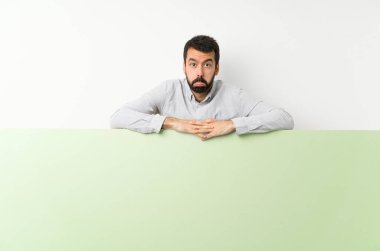 Sakallı genç, yakışıklı bir adam elinde kocaman, boş, üzgün ve depresif bir pankart tutuyor.