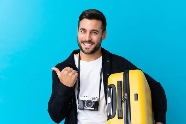 Cestovatel Muž Drží Kufr Přes Izolované Modré Pozadí Ukazuje Strany — Stock fotografie