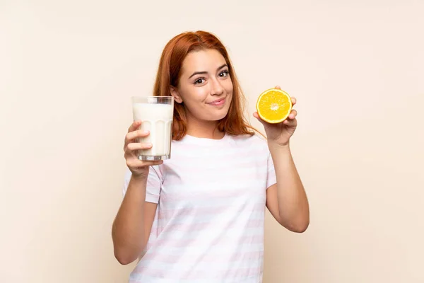 Tinédzser vöröshajú lány kezében egy pohár tejet és egy narancs alatt elszigetelt háttér — Stock Fotó