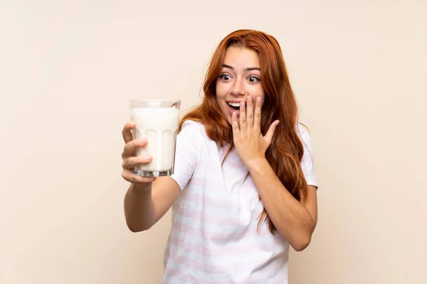 一个红头发少女 在孤零零的背景上端着一杯牛奶 脸上带着惊讶和震惊的表情 — 图库照片