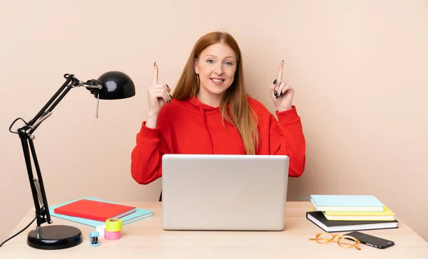 Young student woman in a workplace with a laptop pointing up a great idea