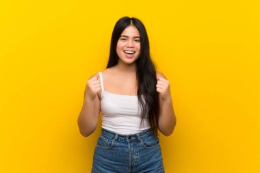 Genç Asyalı kız sarı arka planda zaferi kutluyor.