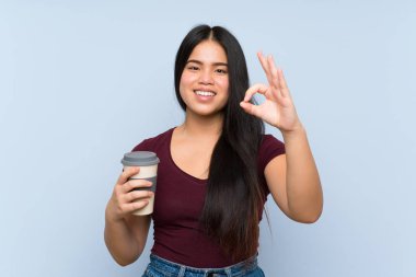 Genç Asyalı kız elinde kahve tutuyor. Parmaklarıyla tamam işareti gösteriyor.