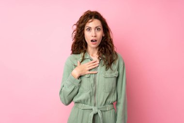 Soyutlanmış pembe arka planı olan genç ve güzel bir kadın şaşırmış ve şaşırmış görünüyor.