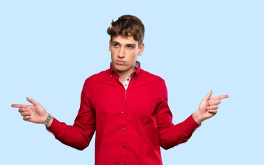 Yakışıklı genç adam, yalıtılmış mavi arka plan hakkında şüpheleri olduğunu gösteriyor.