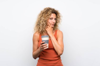 Sarışın, kıvırcık saçlı, elinde kahve tutan genç bir kadın.