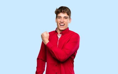 Yakışıklı genç adam izole edilmiş mavi arka planda zaferi kutluyor.