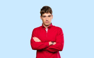 Kollarını çapraz tutan yakışıklı genç adam izole edilmiş mavi arka planda.