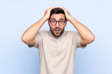 Sakallı, mavi arka planda, yüzünde sürpriz bir ifade olan yakışıklı bir genç.