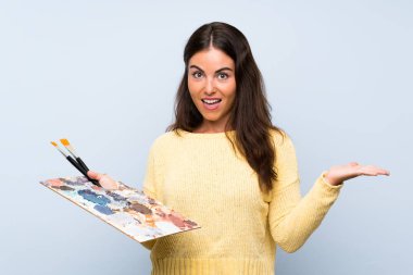 Yüzünde şok ifadesi olan, soyutlanmış mavi arka planda genç bir sanatçı kadın.