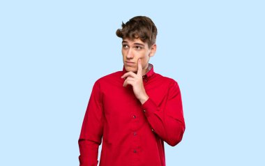 Yakışıklı genç adam, izole edilmiş mavi arka plan üzerine bir fikir düşünüyor.