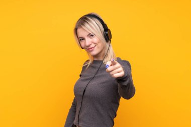 Sarışın bir kadın izole edilmiş sarı arka planda müzik dinliyor ve ön tarafı işaret ediyor.