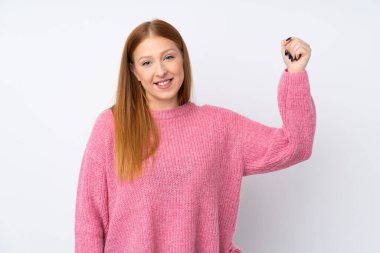 Pembe kazaklı, soyutlanmış beyaz arka planı olan genç, kızıl saçlı kadın güçlü bir jest yapıyor.