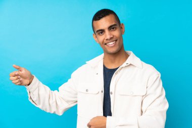 Genç Afro-Amerikalı adam izole edilmiş mavi arka planda gitar hareketi yapıyor.