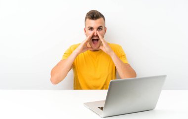 Masada dizüstü bilgisayarı olan genç sarışın adam ağzı açık bağırıyor.