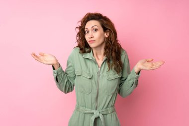 Soyutlanmış pembe arka planda genç ve güzel bir kadın ellerini kaldırırken şüphe duyuyor.