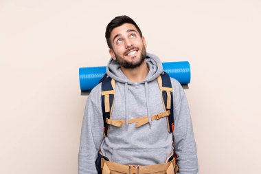 Sırtında büyük bir sırt çantası olan genç dağcı adam izole edilmiş arka planda gülüyor ve yukarı bakıyor