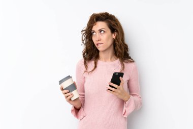 Genç, güzel bir kadın, izole edilmiş arka planda kahve ve bir şeyler düşünürken cep telefonu tutuyor.