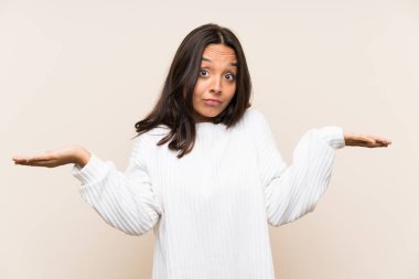 İzole edilmiş arka planda beyaz süveter giyen esmer genç bir kadın. Kafası karışmış bir yüz ifadesi var.