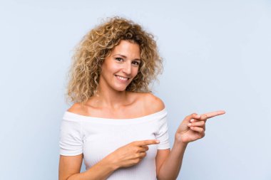 Izole mavi arka plan yan parmak işaret üzerinde kıvırcık saçlı genç sarışın kadın