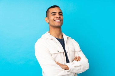 Kollarını kavuşturup ileriye bakan, izole edilmiş mavi bir geçmişi olan genç Afrikalı Amerikalı bir adam.